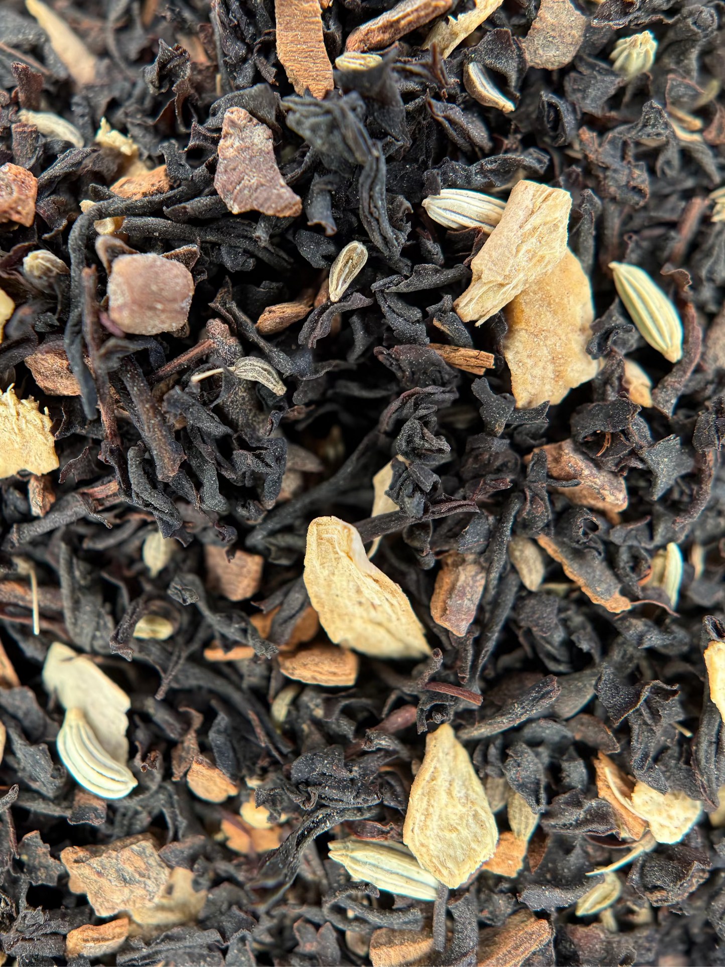 Close-up of loose-leaf herbal tea blend with dark dried tea leaves, light tan citrus slices, and small pale green seed-like pieces.