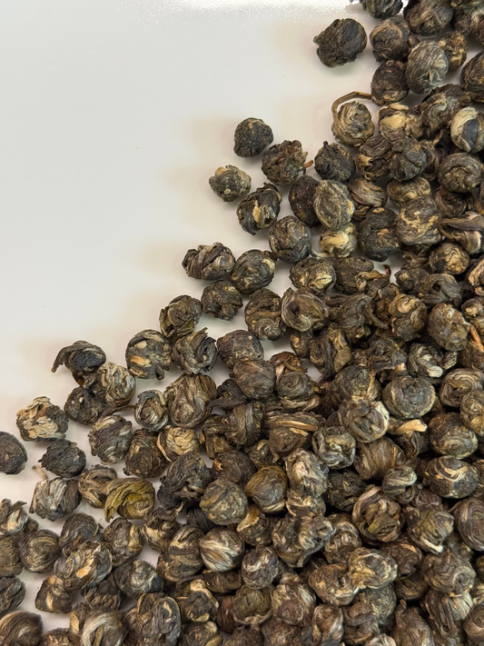 A close-up of rolled dark green to brown tea leaves scattered across a plain white surface.