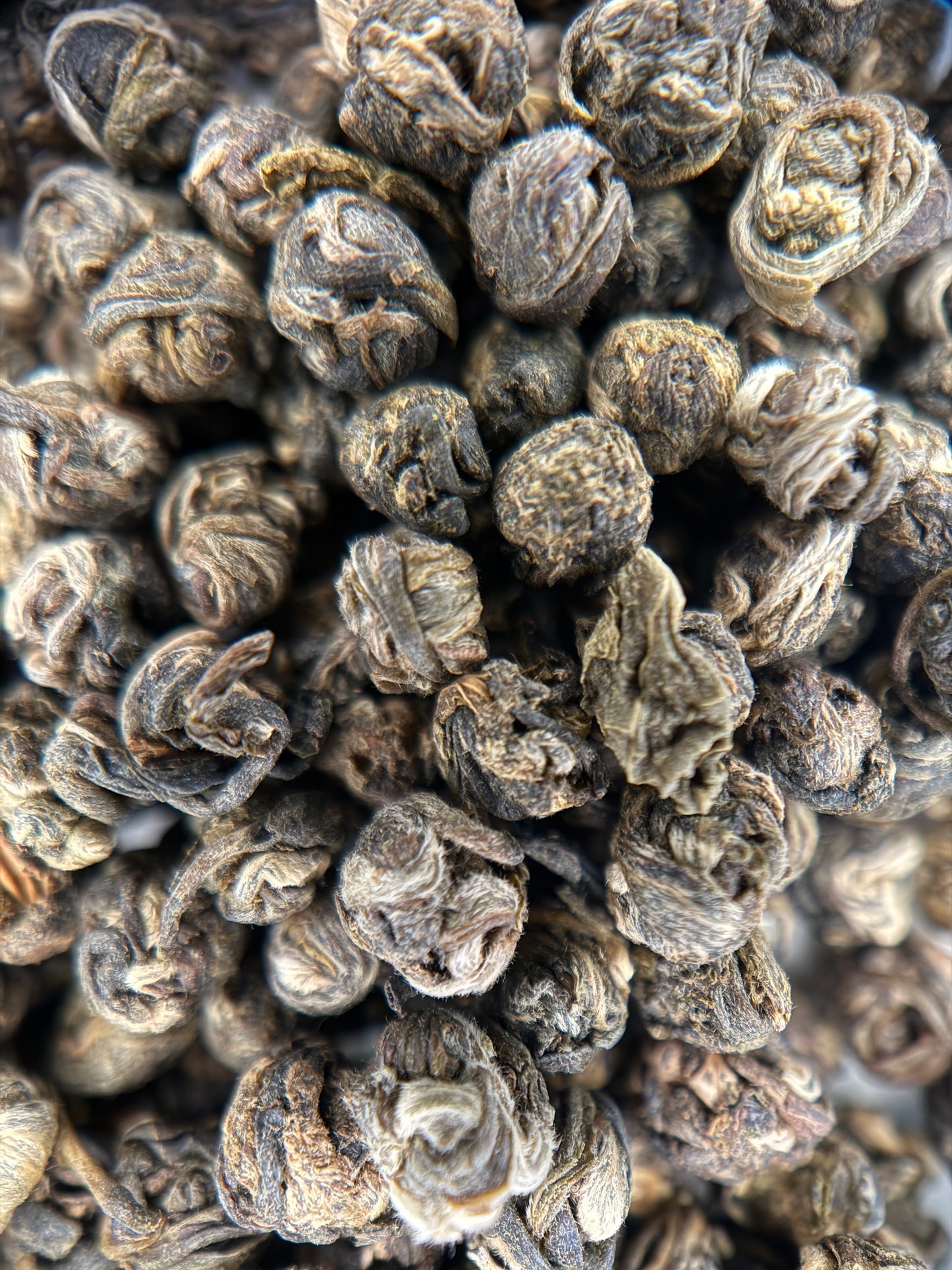 A close-up pile of dried rolled tea leaves, showing their dark brown and gray textured appearance.
