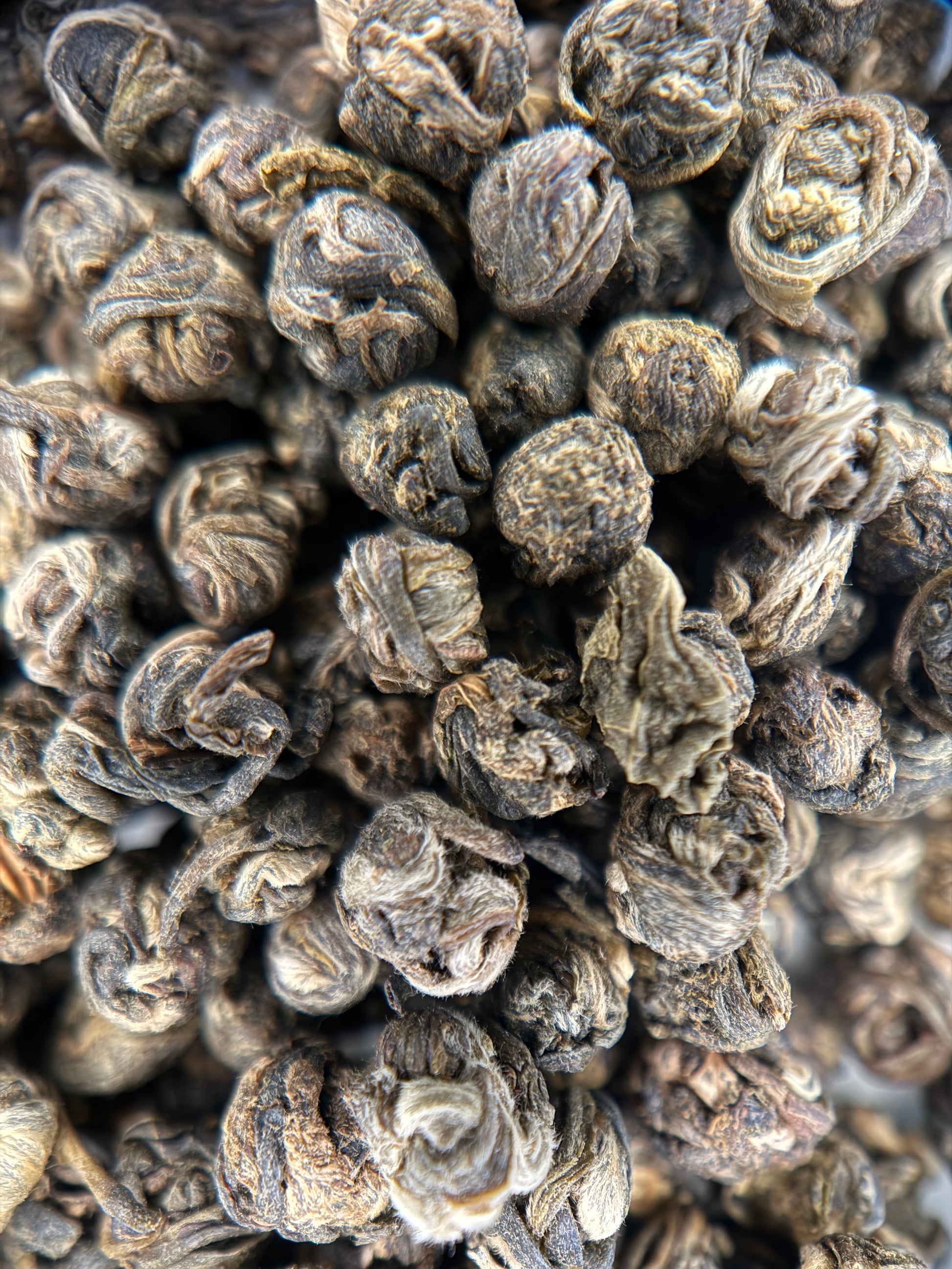 A close-up pile of dried rolled tea leaves, showing their dark brown and gray textured appearance.